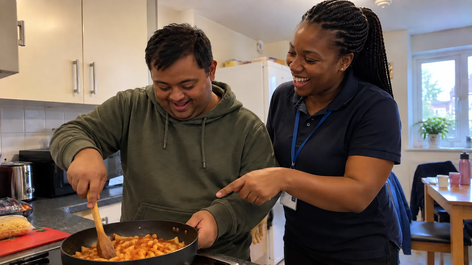 A support worker shows a young man how to cook pasta in his kitchen
